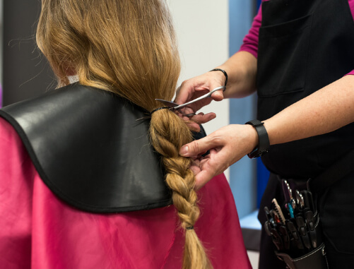  imagem de uma voluntária tendo o cabelo cortado por uma cabeleireira simulando doar os cabelos para ajudar pessoas necessitadas